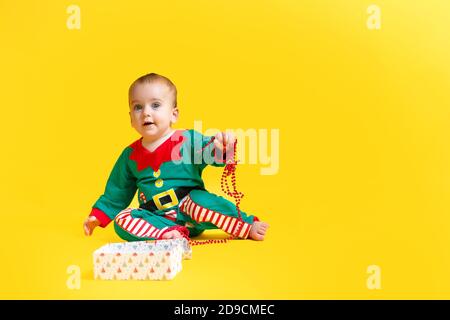 bébé dans santas elf boîte cadeau ouverte sur fond jaune Banque D'Images
