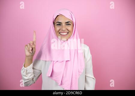 Jeune belle femme arabe portant le hijab islamique sur le rose isolé arrière-plan montrant et pointant vers le haut avec les doigts numéro un sourire confiant Banque D'Images