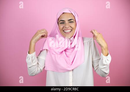 Jeune belle femme arabe portant le hijab islamique sur le rose isolé arrière-plan avec une expression réussie Banque D'Images