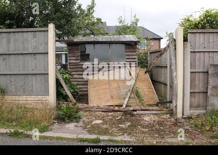 Panneau de clôture endommagé par le vent à l'arrière d'un jardin, révélant un hangar à manilles Banque D'Images