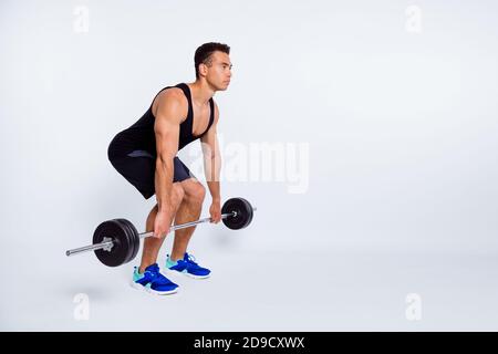 Vue sur toute la longueur du corps de son beau attrayant content sportive forte focalisé gars qui fait l'exercice lever barbell effort isolé Banque D'Images