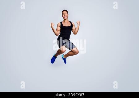 Vue sur toute la longueur du corps de son beau attrayant sportif musclé gai heureux gars sauter célébrant la grande réalisation se réjouir isolé Banque D'Images