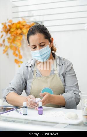 Chef pâtissier travaillant avec fondant pour décorer un gâteau - Femme cuisinant avec masque - femme peignant de l'argile avec des teintures Banque D'Images