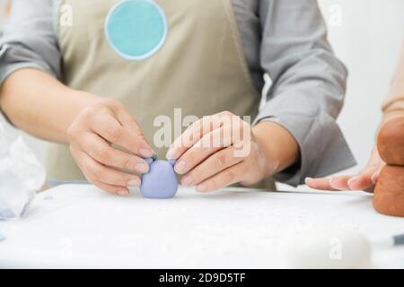Gros plan des mains de femme travaillant avec fondant pour décorer un gâteau - femme peinture argile avec pinceau et teintures - femme artisan Banque D'Images
