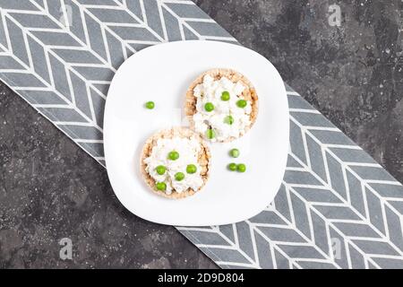 Pains croustillants au fromage cottage et petits pois verts sur un blanc plaque sur fond gris Banque D'Images