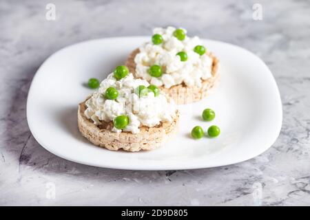 Pains croustillants au fromage cottage et petits pois verts sur un blanc plaque Banque D'Images