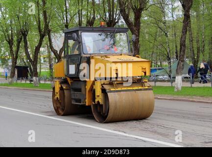 La patinoire d'asphalte est jaune avec des roues de fer sur la route de la ville sur fond d'arbres verts. Travaux de réparation dans la rue sur la pose d'asphalte. Banque D'Images