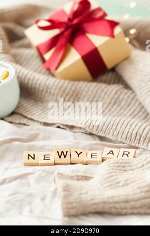 inscription nouvel an sur tissu beige froissé, boîte cadeau avec ruban rouge, guirlande sur pull beige sur fond. carte du nouvel an festive et confortable, Banque D'Images