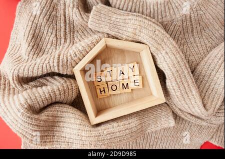 restez à la maison, lettrage en lettres carrées en bois dans petite maison en bois sur pull beige. Image monochrome, avertissement pour la période de la seconde Banque D'Images
