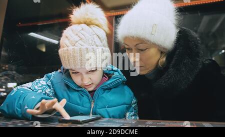 Jolie mère et fille caucasienne avec smartphone assis dans un café. Un petit enfant avancé montre et explique à maman quelque chose sur le smartphone. Banque D'Images