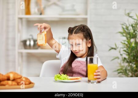 l'enfant ne veut pas prendre le petit déjeuner. la petite fille regarde le sandwich avec dégoût Banque D'Images