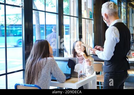 Serveur caucasien prenant la commande de clients dans un restaurant pendant l'épidémie de coronavirus. Nouvelle norme dans les restaurants. Pandémie de coronavirus. Banque D'Images