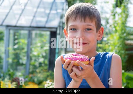 Enfant heureux tenant un donut rose dans le parc. L'enfant refuse de manger des aliments sains. Concept alimentaire malsain Banque D'Images