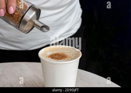 Gros plan d'une main de femme versant le sucre brun d'un distributeur dans une tasse en plastique blanc avec du thé ou du café Banque D'Images