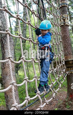 Garçon surmontant l'obstacle de mesh dans le parc d'aventure de la forêt, Carélia Banque D'Images