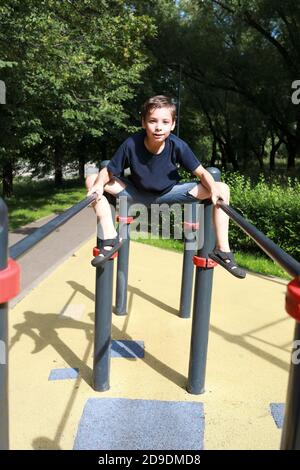 L'enfant forme les muscles abdominaux sur des barres irrégulières dans le parc Banque D'Images