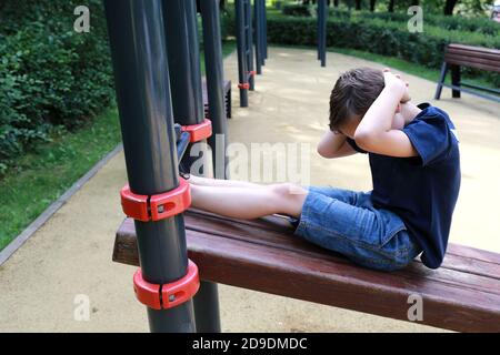 L'enfant forme les muscles abdominaux sur le simulateur dans le parc Banque D'Images