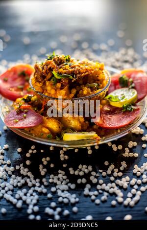Gros plan de sabudana khichdi épicé ou de balle sago khichdi avec quelques tomates en tranches, quelques citrons coupés dans une assiette de verre, et de sago bal cru Banque D'Images