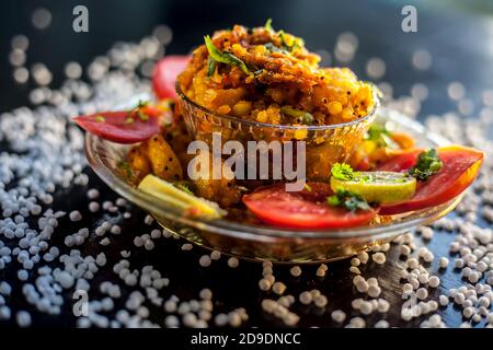 Gros plan de sabudana khichdi épicé ou de balle sago khichdi avec quelques tomates en tranches, quelques citrons coupés dans une assiette de verre, et de sago bal cru Banque D'Images