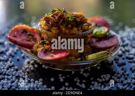 Gros plan de sabudana khichdi épicé ou de balle sago khichdi avec quelques tomates en tranches, quelques citrons coupés dans une assiette de verre, et de sago bal cru Banque D'Images