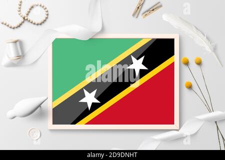 Drapeau de Saint-Kitts-et-Nevis dans un cadre en bois sur fond blanc créatif. Thème blanc, plumes, Marguerite, bouton, objets ruban. Banque D'Images