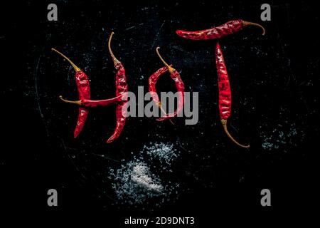 CHAUD écrit sur une surface noire avec l'aide de quelques rouges chauds. Photo de haut en haut des chilines rouges chaudes qui font le mot chaud. Banque D'Images