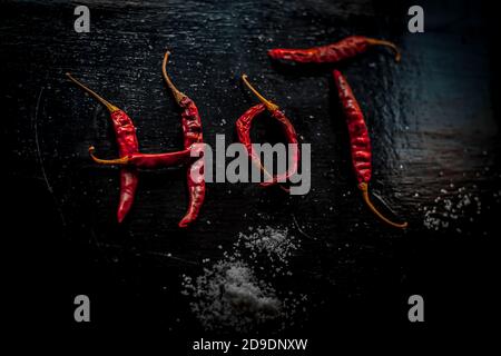 CHAUD écrit sur une surface noire avec l'aide de quelques rouges chauds. Photo de haut en haut des chilines rouges chaudes qui font le mot chaud. Banque D'Images