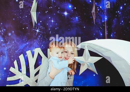 Jeune femme blonde en vêtements décontractés posant avec un petit garçon sur fond de Noël de lune blanche et de ciel bleu. Banque D'Images