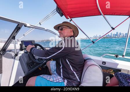 Un australien portant un chapeau, des lunettes de soleil et un gilet de protection contre les éruptions cutanées, conduisant un bateau ouvert dans le port de Sydney, en Australie Banque D'Images