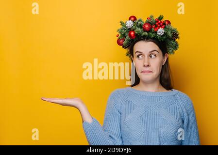 La jeune femme hésitante a surpris l'expression sans indice, regarde la paume relevée à la surprise, fait face à la situation difficile, porte une couronne faite à la main Banque D'Images