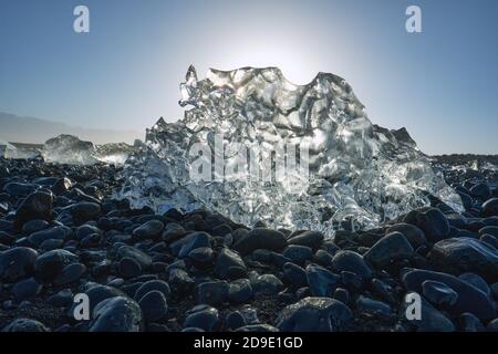 Fusion des fragments glaciaires de l'iceberg sur la plage de galets de basalte noir De Jokulsarlon Islande - glace de fonte du soleil - réchauffement de la planète - changement climatique Banque D'Images