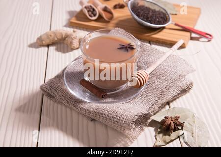 Une tasse de thé indien chaud masala thé, cuillères avec épices sur une planche à découper, sur un fond blanc. Orientation horizontale. Banque D'Images