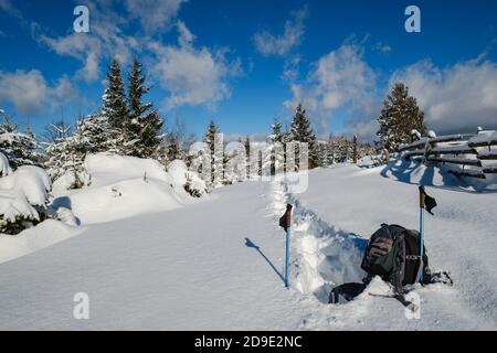 En hiver, en bordure de village alpin isolé, la neige dévie sur le bord de la forêt de sapins de montagne. Sac à dos touristique sur un sentier de randonnée fraîchement trodden. Banque D'Images