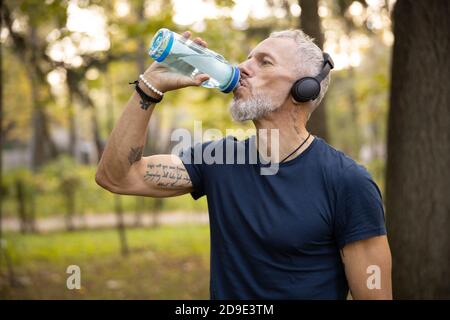 Homme sportif qui boit de l'eau pendant l'entraînement à l'extérieur Banque D'Images