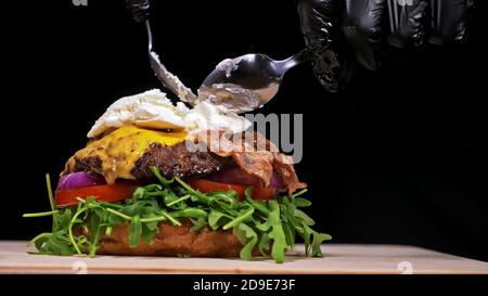 Burger d'artisanat est cuisson sur fond noir. Composé : sauce, roquette, tomate, oignon, bacon, fromage ricotta, sauce au cassis, pain d'air et en viande. Banque D'Images