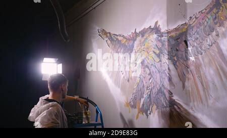 Concepteur de l'artiste dessine un aigle sur le mur. Décorateur artisan photo peintures à l'acrylique couleur d'huile. Peintre peintre vêtu de couche de peinture. À l'intérieur. Banque D'Images