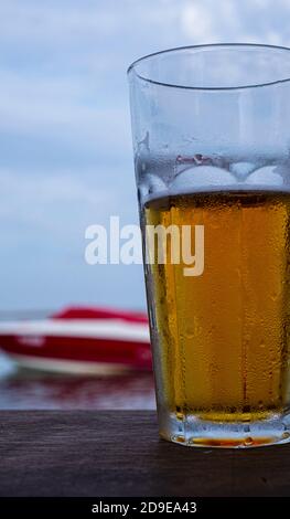 Verre de bière dorée sur la plage sur fond d'eau et d'un bateau. Banque D'Images