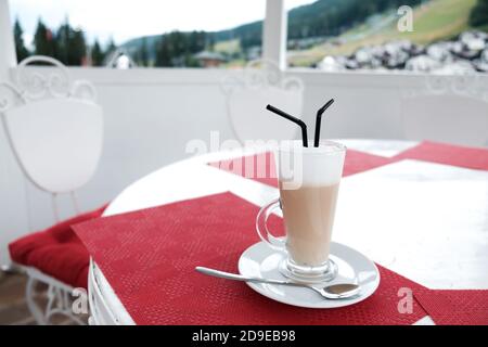 Tasse de café latte en verre avec deux pailles en plastique sur une table à l'extérieur. Il sert des boissons caféinées dans une cafétéria. Service de restauration magnifique. Banque D'Images