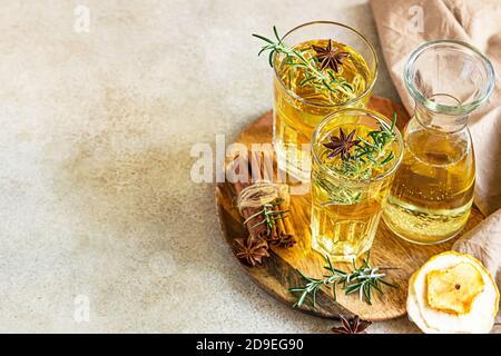 Poire ou cidre de pomme en verres et bouteille avec romarin, cannelle et poires bio fraîches. Boisson aux fruits fermentés. Arrière-plan béton clair. Vue de dessus. Banque D'Images