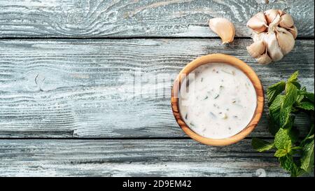 Authentique sauce raita au concombre pakistanais sur fond de bois gris. Sauce raita trempée avec des compléments de concombre, d'oignon et de tomate dans un petit bol en métal et un pot en verre. Vue de dessus ou plan de travail. Copier l'espace. Bannière Banque D'Images