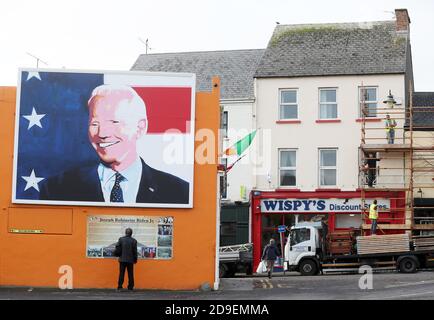 Un homme s'arrête pour lire une plaque sous une fresque du candidat à la présidence des États-Unis Joe Biden dans sa maison ancestrale de Ballina, Co. Mayo, Irlande, où il s'est rendu en juin 2016 en tant que vice-président. Banque D'Images