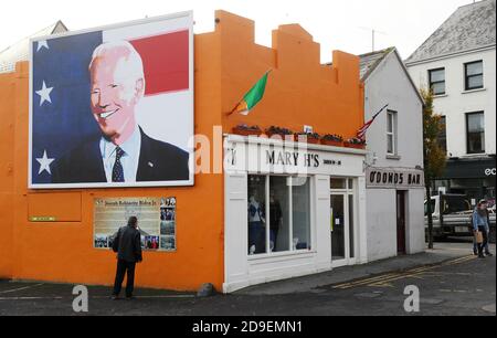 Un homme s'arrête pour lire une plaque sous une fresque du candidat à la présidence des États-Unis Joe Biden dans sa maison ancestrale de Ballina, Co. Mayo, Irlande, où il s'est rendu en juin 2016 en tant que vice-président. Banque D'Images