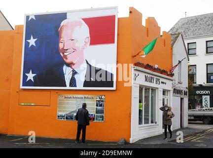 Un homme s'arrête pour lire une plaque sous une fresque du candidat à la présidence des États-Unis Joe Biden dans sa maison ancestrale de Ballina, Co. Mayo, Irlande, où il s'est rendu en juin 2016 en tant que vice-président. Banque D'Images