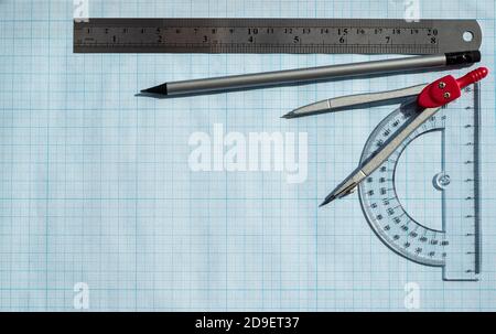 Cadre composé d'accessoires pour les calculs et le dessin sur papier graphique bleu. Règle de rapporteur simple crayon et compas. Sciences exactes. Banque D'Images