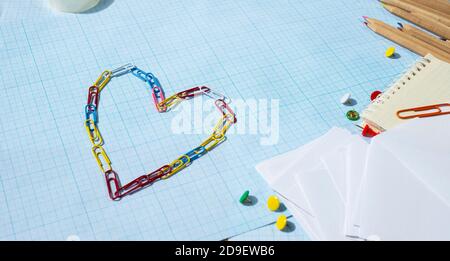 Papier punaises crayons et un coeur fait de trombones de couleur. Espace libre pour le texte. Banque D'Images