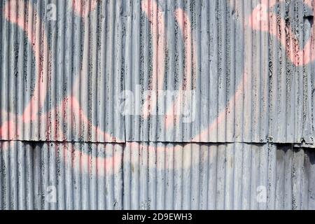 L'écaillage de la peinture gris et rose graffiti sur un mur de métal ondulé Banque D'Images