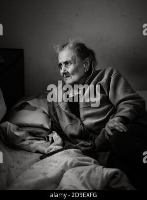 Portrait noir et blanc d'un très vieux et fatigué de la vie ridée femme couché sur le lit et regardant TÉLÉVISION Banque D'Images