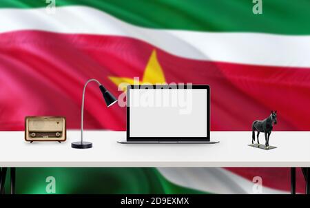 Drapeau national du Suriname avec espace de travail, ordinateur de bureau et accessoires de bureau sur table blanche moderne. Banque D'Images