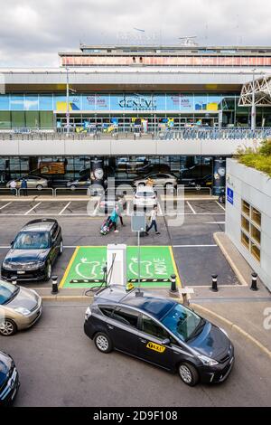 Des taxis attendent les clients sur le parking de l'aéroport international de Genève, tandis que les personnes qui tirent des bagages se dirigent vers l'entrée. Banque D'Images