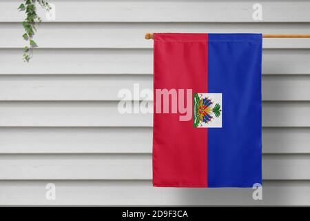 Le petit drapeau national d'Haïti est suspendu d'une clôture de piquetage le long du mur en bois dans une ville rurale. Concept de jour d'indépendance. Banque D'Images